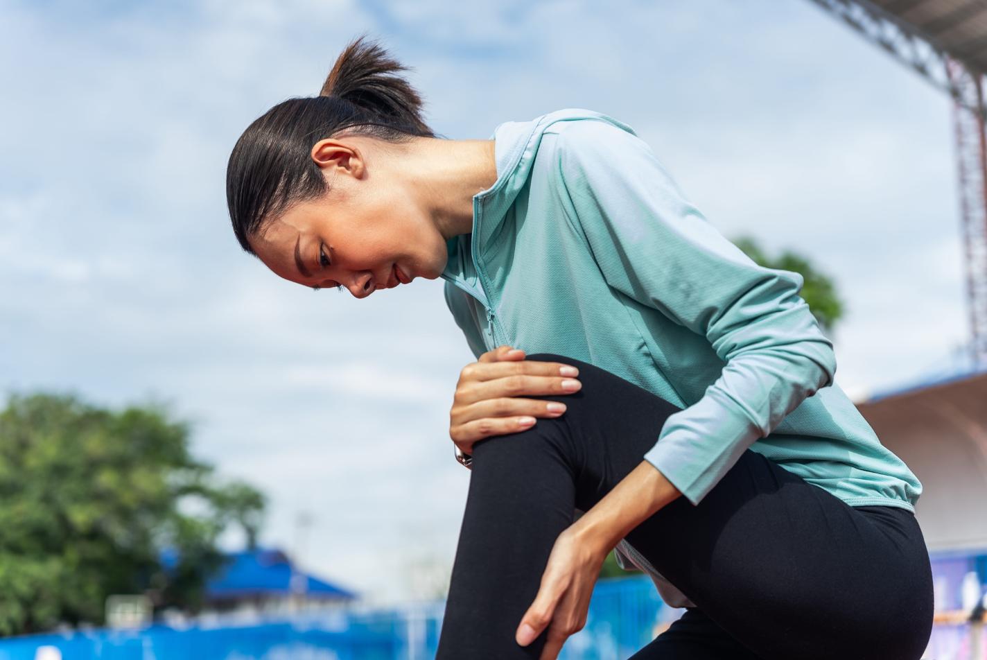 A young woman massages her left calf during a training run. Regular massage for runners helps