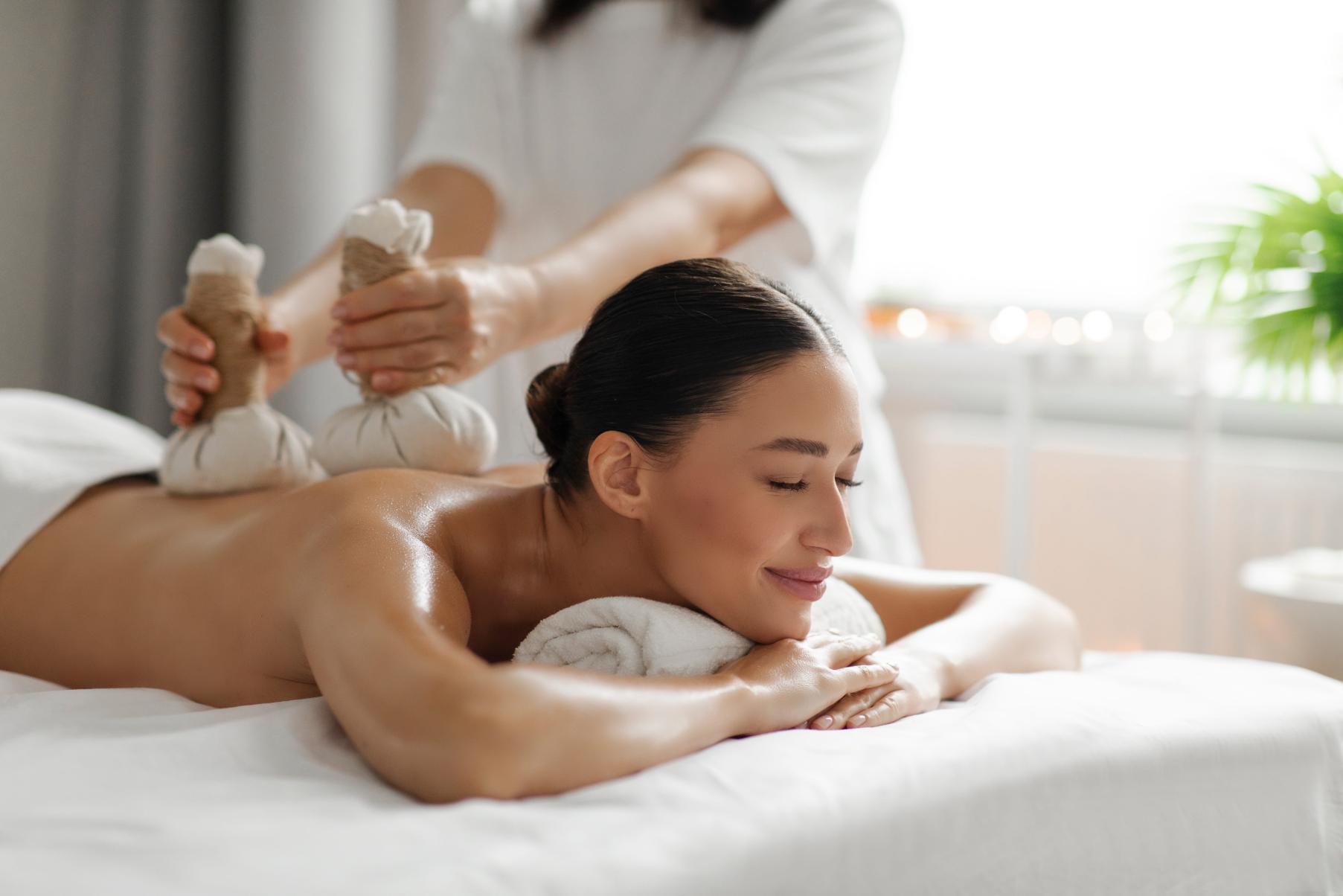 A young woman enjoying a Thai herbal massage, with compresses used for a warm, calming spa session.