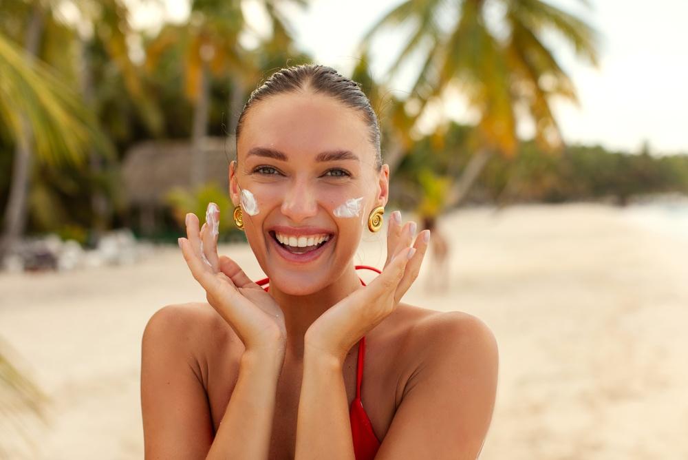 A happy woman applying sunscreen on her face