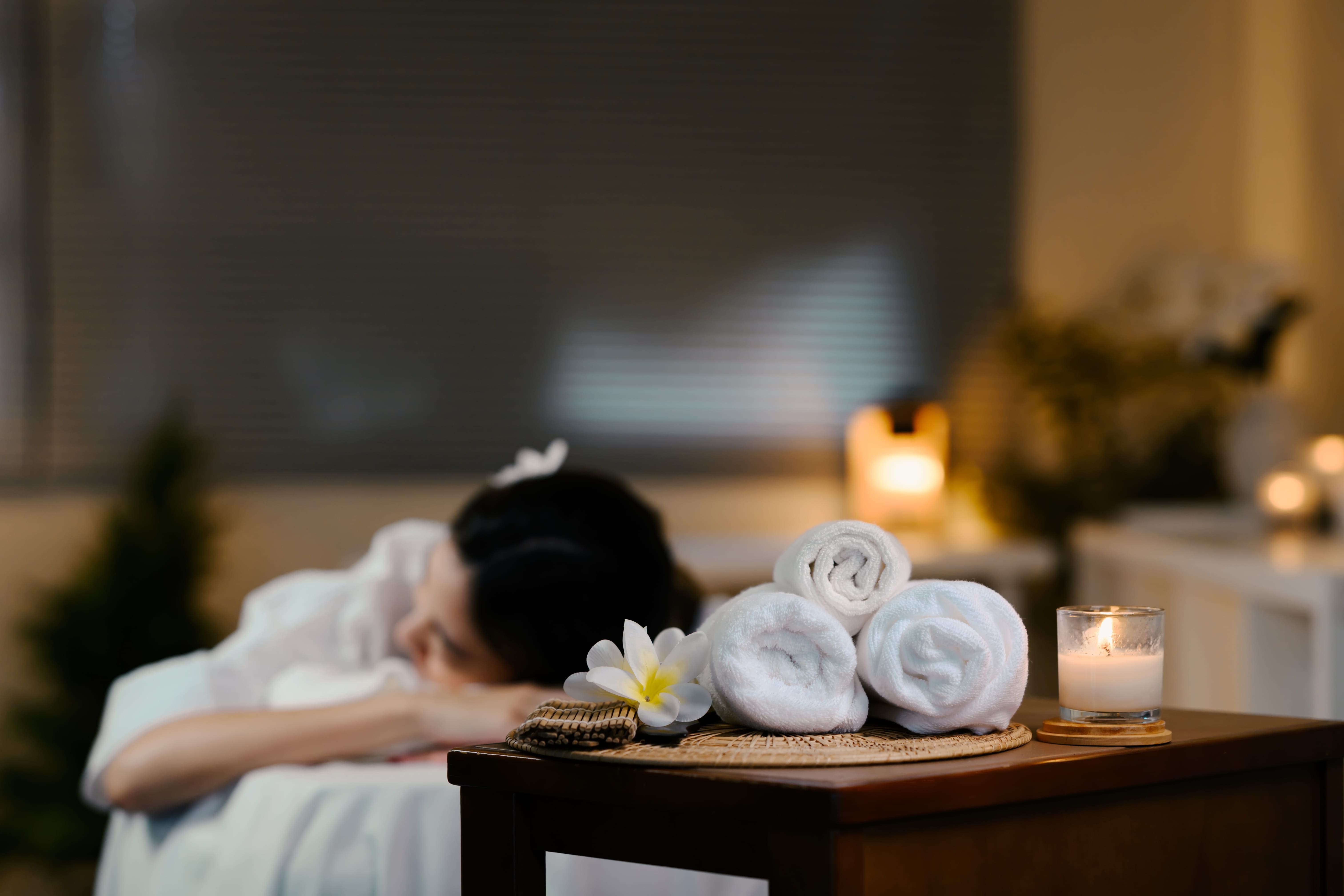 A calm spa room set up with rolled towels and a candle while a guest relaxes