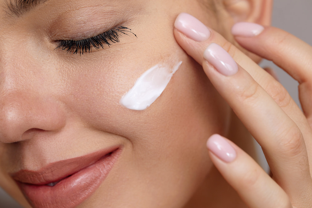 A woman smiling and applying a cream to her face for her skin cycling routine
