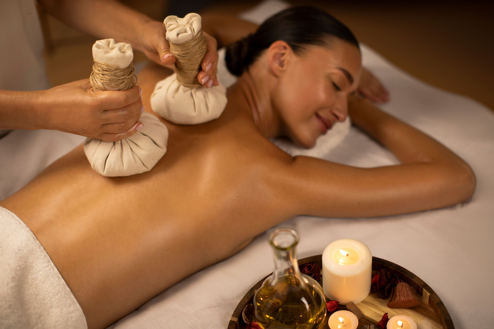 woman laying on her stomach receives a herbal compress as part of a body treatment