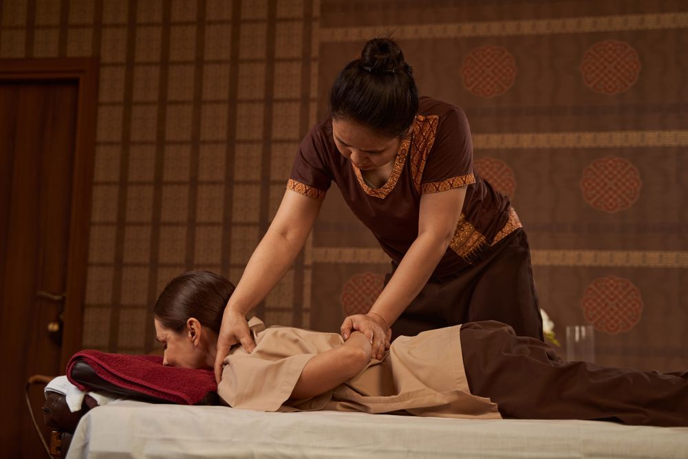 Thai therapist in traditional dress applying palm pressure to a guest's back