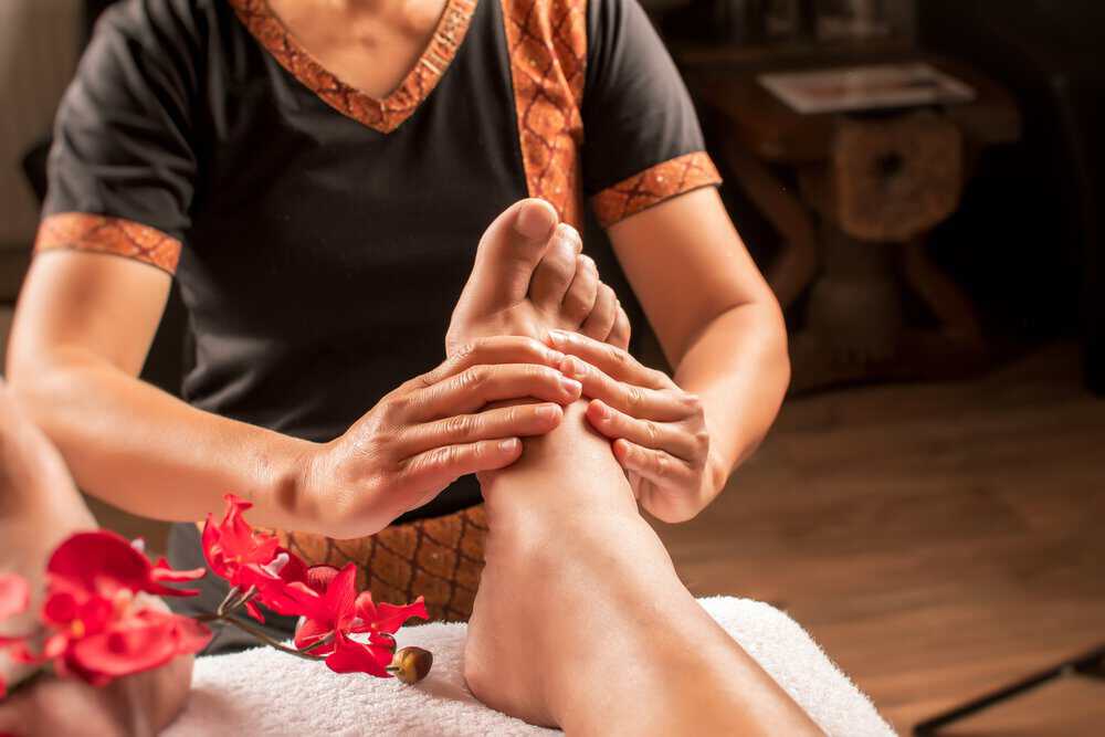 Female massage therapist uses two hands to massage a patient’s foot with acupressure