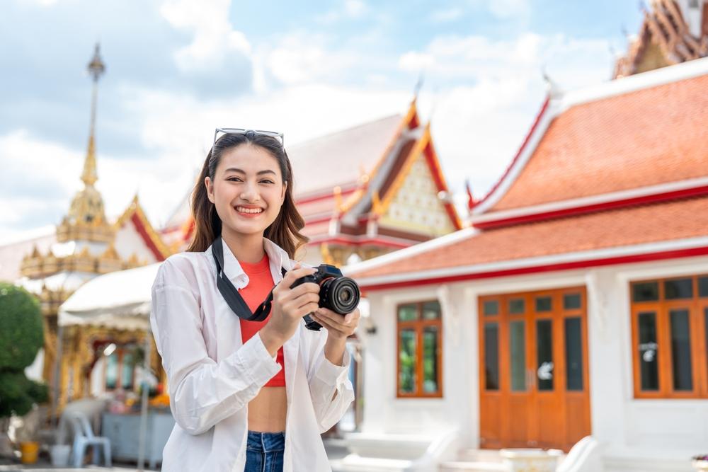 A young woman with a backpack taking photos on temple grounds; one of many best places to visit in Thailand.