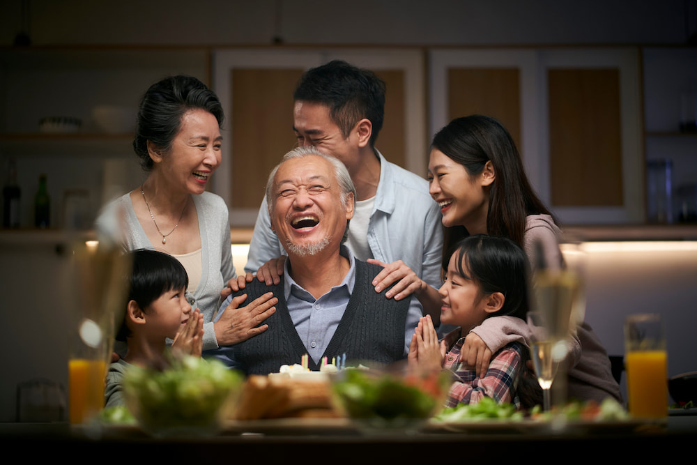 A happy three-generation family laughs together at a birthday celebration at home