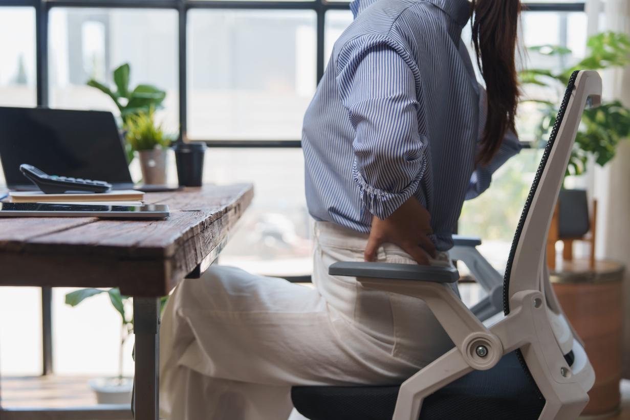 A woman sitting at her office desk holding her lower back in pain